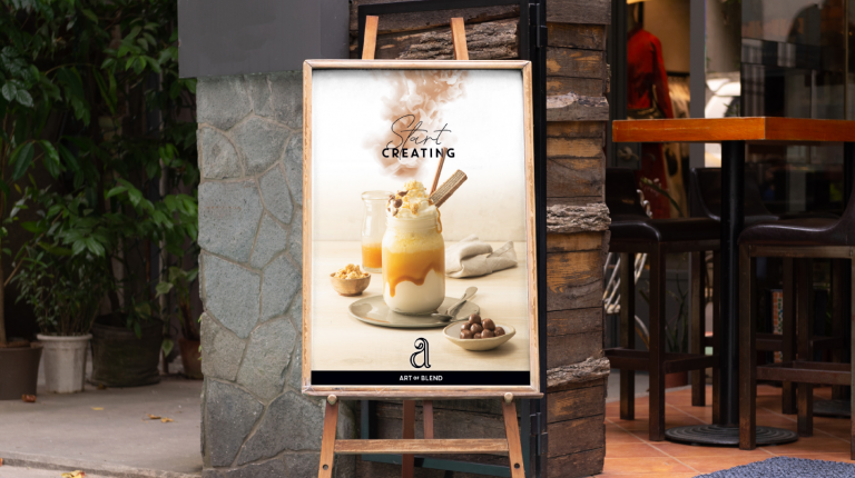 A poster for Art of Blend on a stand outside a coffee shop. The poster features a caramel frappe drink with whipped cream and a straw.