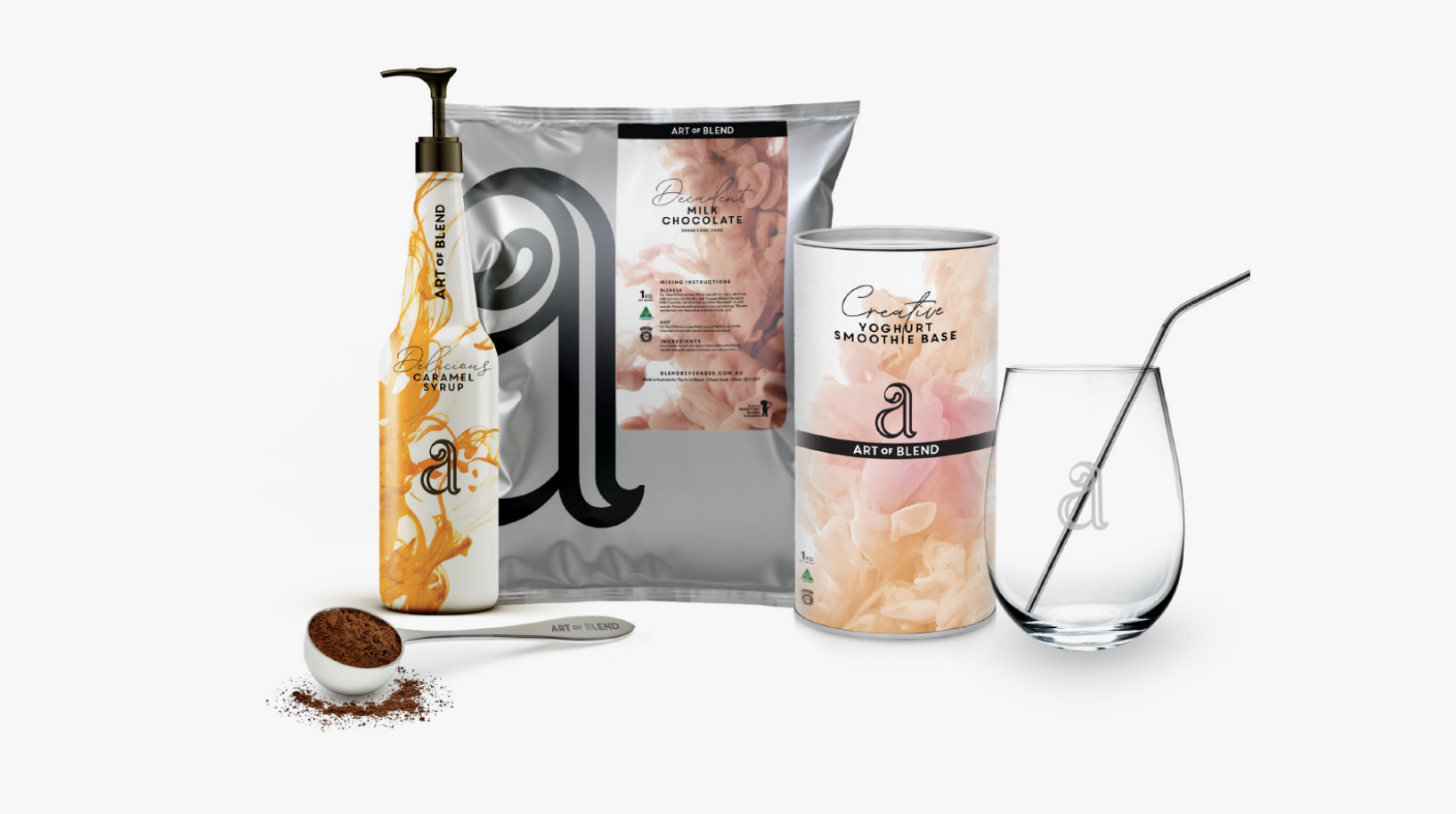 A setup of Art of Blend packaging featuring a caramel syrup bottle, a milk chocolate drink mix pack, a yogurt smoothie base bag, a cup, and a scooper.